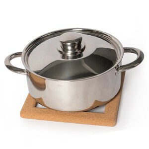 Puede incluir: Una olla de acero inoxidable con tapa sobre una base de corcho.
