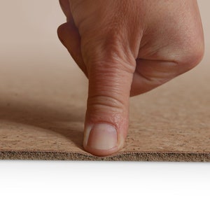 May include: A close-up of a finger pressing down on a brown cork yoga mat. The mat is flexible and has a textured surface.