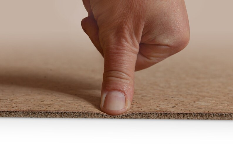 May include: A close-up of a finger pressing down on a brown cork yoga mat. The mat is flexible and has a textured surface.