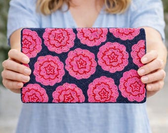 May include: A navy blue beaded clutch with a repeating pattern of pink and red flowers. The flowers have a detailed, textured appearance, and the clutch is rectangular in shape.