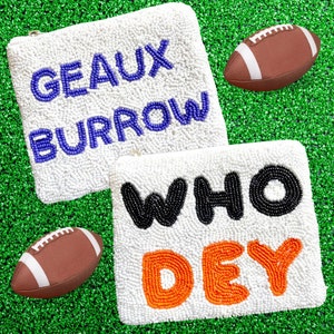 May include: Two white beaded pouches with different phrases. The top pouch has the words "GEAUX BURROW" in purple beads. The bottom pouch has the words "WHO DEY" in black and orange beads. Two brown footballs are on either side of the pouches.