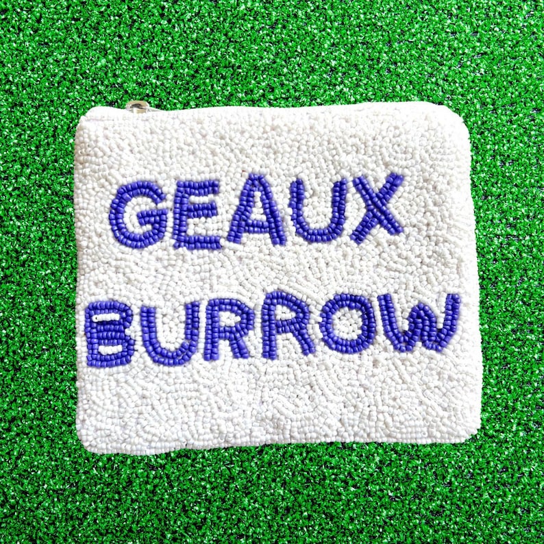 May include: White beaded pouch with a zipper closure. The pouch has the words "GEAUX BURROW" in purple beads.