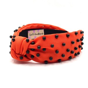 May include: Orange knotted headband with black beads. The headband has the text "Saints Headbands" on the side.