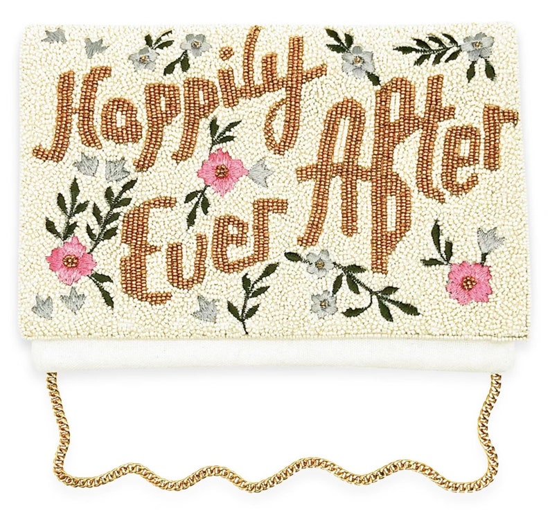 May include: A white beaded clutch with a gold chain strap. The clutch is decorated with gold beads that spell out "Happily Ever After" and pink and white floral embroidery.