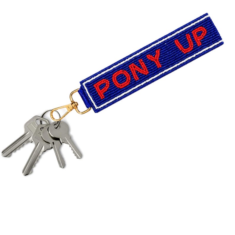 May include: A rectangular beaded keychain strap in royal blue with white border stripes and the text PONY UP in red beads. The strap is attached to a gold-toned metal lobster clasp holding a cluster of four silver-colored metal keys.