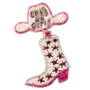 May include: A beaded patch featuring a white cowboy hat with pink trim and the text "LET'S GO GIRLS" in red, connected to a white cowboy boot with red star accents and a pink heel, all crafted with small, reflective glass beads on a white background.