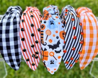 May include: Five knotted headbands featuring various patterns: black and white buffalo check, orange and white stripes with black rhinestones, a white Halloween print with ghosts and bats, black and white stripes with orange rhinestones, and orange gingham.