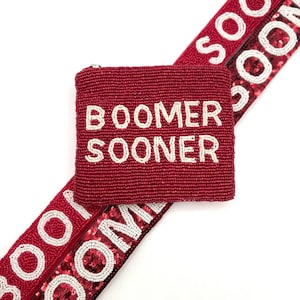 May include: A burgundy beaded coin purse with the words "BOOMER SOONER" in white beads. Two burgundy sequined straps with the words "SOONER" in white beads are also visible.