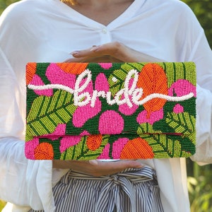 May include: A beaded clutch bag with a tropical floral pattern in shades of green, pink, and orange. The word "bride" is spelled out in white beads on the front of the bag.