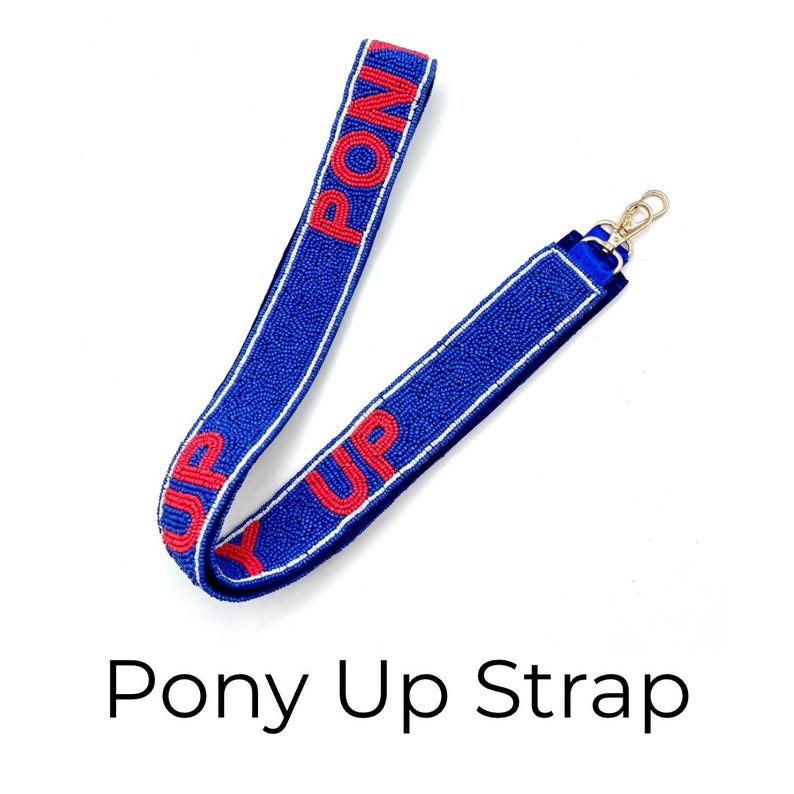 May include: A blue beaded strap featuring the text PONY UP in red beads. The strap is bordered by thin white lines and includes a gold-toned metal lobster clasp at one end. The design consists of small, uniform beads covering the entire surface.