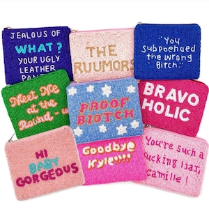 May include: A collection of beaded coin purses in various colors, including blue, pink, green, and fuchsia. Each purse features a different phrase or word, such as "Jealous of What?" and "Bravo Holic."