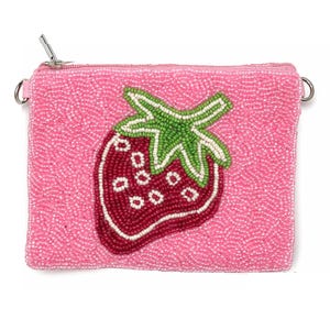 May include: Pink beaded clutch with a strawberry design. The clutch features a zipper closure and a silver chain strap. The strawberry is red with white seeds and green leaves. The background is a solid pink color.