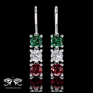 May include: A pair of silver-toned drop earrings featuring three vertically aligned round-cut stones in green, clear, and red. Each stone is held in a four-prong setting, suspended from a silver-toned leverback hook against a black background.