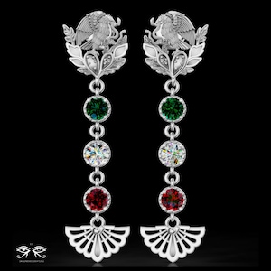 May include: A pair of silver drop earrings featuring a top eagle emblem, followed by a vertical chain of three round faceted stones in green, clear, and red, ending with a silver fan-shaped pendant at the base. The logo text is visible at the bottom.