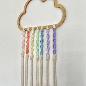 Puede incluir: Una pared de madera en forma de nube con hilos de lana multicolores en arcoíris que cuelgan de ella.