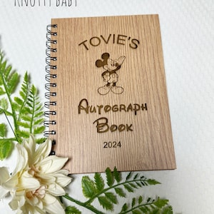 Könnte beinhalten: Ein Autogrammbuch aus Holz mit einem Mickey-Mouse-Motiv. Das Buch ist mit dem Text "Tovie's Autograph Book 2024" graviert.