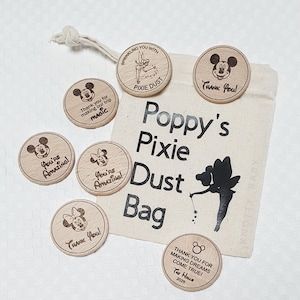 Op de afbeelding: Een set houten tokens met een Mickey Mouse en Tinkerbell-thema. De tokens hebben verschillende spreuken, waaronder "You're Amazing!" en "Thank You!" De tokens zitten in een kleine jute zak met de tekst "Poppy's Pixie Dust Bag" erop gedrukt.