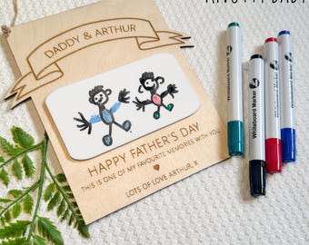 May include: A wooden Father's Day gift with a banner that reads "DADDY & ARTHUR". The gift features a drawing of two stick figures and the text "HAPPY FATHER'S DAY". Includes whiteboard markers. The text "NEW PERSONALISED DRAWING BOARDS" is also visible.
