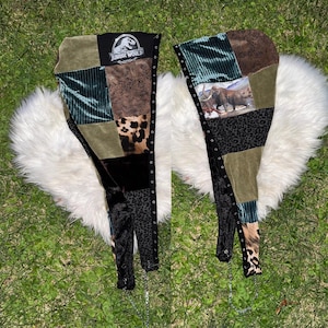 May include: A pair of patchwork leg warmers featuring various fabric textures including green velvet, brown animal print, and black leopard print. One leg warmer displays a Jurassic World logo, while the other features a graphic of a mammoth.