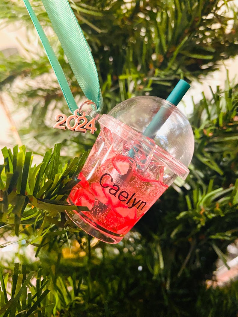 Puede incluir: Un vaso de pl&aacute;stico transparente con un l&iacute;quido rojo y una pajita verde. El vaso tiene el nombre "Caelyn" escrito en &eacute;l y el a&ntilde;o "2024" est&aacute; unido a la parte superior del vaso.