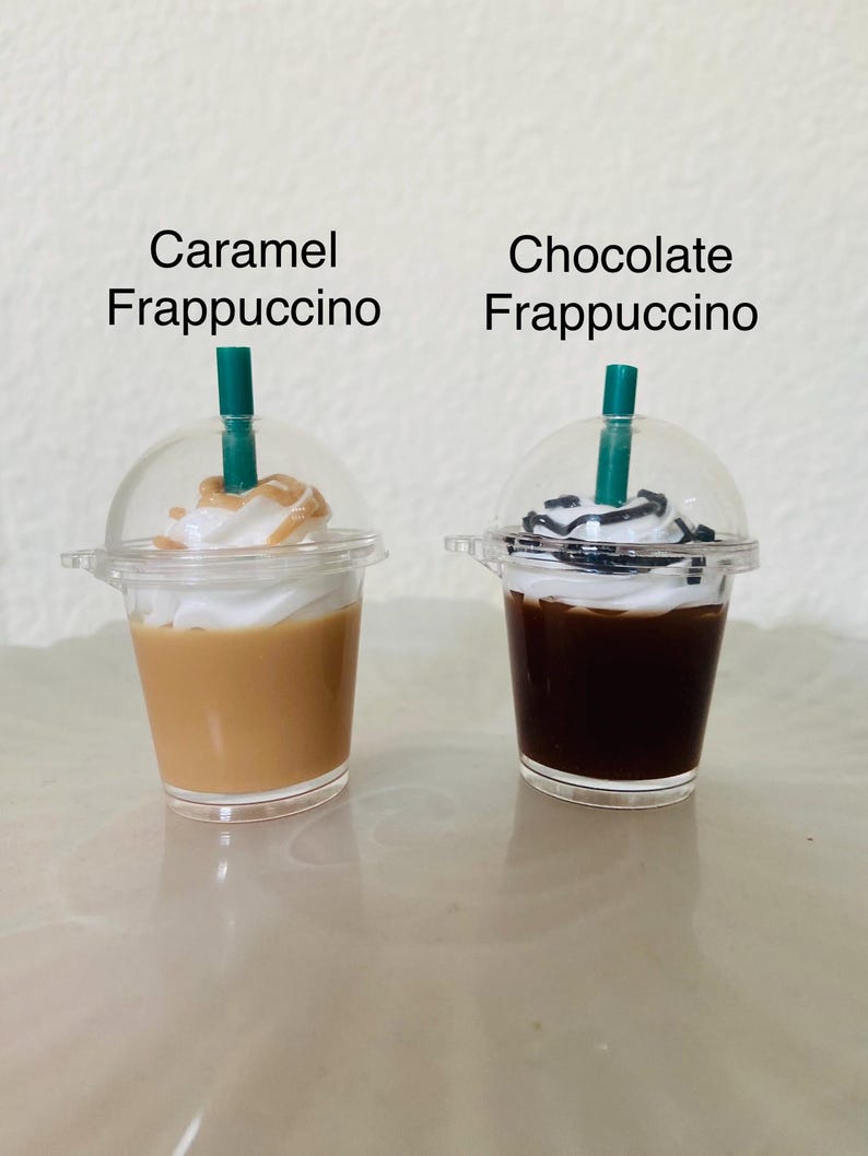 Puede incluir: Dos vasos de pl&aacute;stico en miniatura con tapas y pajitas, llenos de una bebida con sabor a caramelo y chocolate. Los vasos est&aacute;n etiquetados como "Caramel Frappuccino" y "Chocolate Frappuccino".