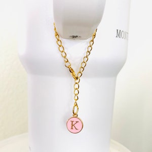 May include: A gold chain with a pink circle charm featuring the letter "K" in gold.