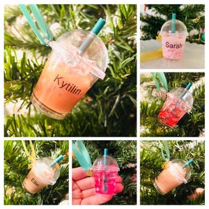 Puede incluir: Seis adornos navide&ntilde;os personalizados con forma de vasos de pl&aacute;stico transparente con tapas y pajitas. Cada vaso est&aacute; lleno de un l&iacute;quido de color diferente y tiene un nombre escrito en el lateral. Los nombres son Kytilin, Sarah, Caelyn, Ellie, Kylie y un sexto nombre que no es visible.