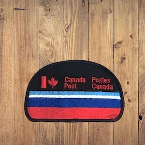 May include: A black, semi-circular patch with the text "Canada Post" and "Postes Canada" in red. The patch features a red maple leaf and a red, white, and blue striped design.