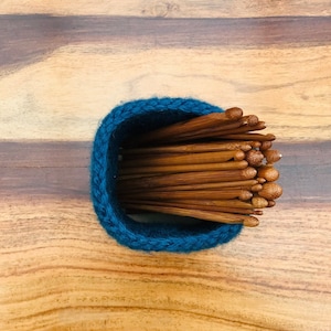 Peut inclure: Un porte-aiguilles à tricoter en crochet bleu rempli d'un grand nombre d'aiguilles à tricoter en bois.
