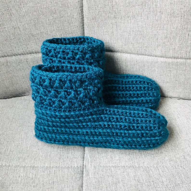 K&ouml;nnte beinhalten: Ein Paar tealblaue geh&auml;kelte Hausschuhe. Die Socken sind mit einem strukturierten Stich gearbeitet und haben einen umgeschlagenen Bund.