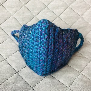 Op de afbeelding: Een blauw en paars gebreid gezichtsmasker met twee oorlussen.