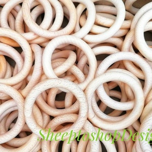 Könnte beinhalten: Nahaufnahme eines Haufens unfertiger Holzringe. Die Ringe haben eine helle, natürliche Holzfarbe mit sichtbarer Maserung. Die Ringe sind kreisförmig und scheinen glatt zu sein. Das Bild ist gut beleuchtet und hebt die Textur und die Details des Holzes hervor.