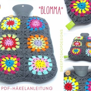 May include: A gray crocheted hot water bottle cover with colorful floral designs. The cover features a grid pattern with bright pink, yellow, blue, and orange flowers. The text "BLOMMA" is visible.