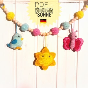 Könnte beinhalten: Ein Häkel-Babymobil mit einem gelben Stern, einem rosa Schmetterling und einem blauen Vogel. Das Mobile ist aus Holzperlen gefertigt und hat einen Clip zum Befestigen an einem Kinderbett oder Kinderwagen. Der Text auf dem Bild lautet "PDF - Häkelanleitung Kinderwagenkette "SONNE""