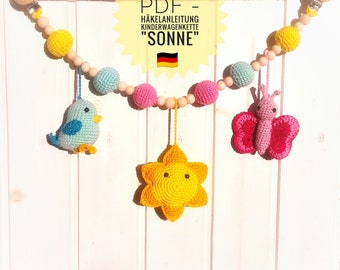 May include: A crochet baby mobile with a yellow star, a pink butterfly, and a blue bird. The mobile is made with wooden beads and has a clip for attaching to a crib or stroller. The text on the image reads "PDF - Häkelanleitung Kinderwagenkette "SONNE""