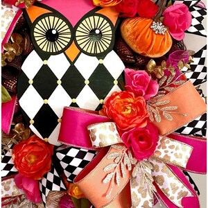 May include: A black and white checkered wreath with a pink and orange bow. The wreath features a painted owl with large eyes and a small orange pumpkin. The wreath is decorated with pink, orange, and gold flowers.