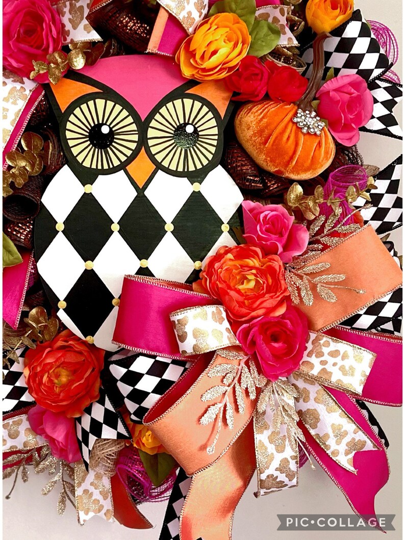 May include: A black and white checkered wreath with a pink and orange bow. The wreath features a painted owl with large eyes and a small orange pumpkin. The wreath is decorated with pink, orange, and gold flowers.