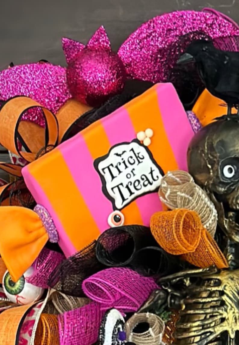 May include: A pink and orange striped candy-shaped Halloween wreath with a "Trick or Treat" sign, black and orange mesh, a black crow, and a gold skeleton.