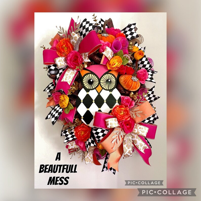 May include: A pink and black owl with a checkered pattern is the centerpiece of this fall wreath. The wreath is decorated with pink, orange, and gold ribbons, as well as faux flowers and pumpkins. The text "A Beautiful Mess" is visible at the bottom of the wreath.