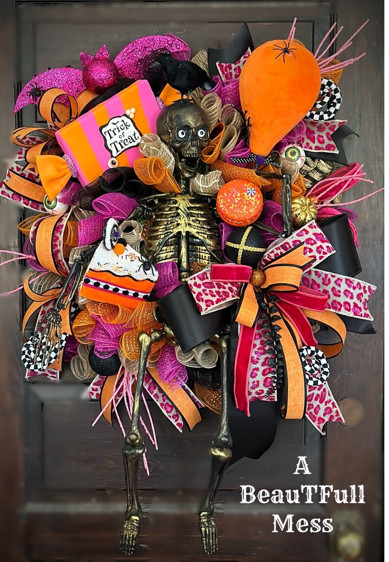 May include: A Halloween wreath featuring a skeleton holding a candy box that says "Trick or Treat". The wreath is decorated with pink, orange, and black ribbons, along with other Halloween-themed decorations.