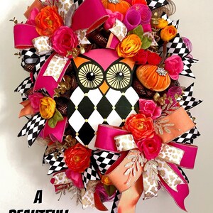 May include: A black and white checkered owl with pink accents, surrounded by pink, orange, and gold ribbon and floral accents. The wreath is decorated with small pumpkins and has the text "A Beautiful Mess" at the bottom.