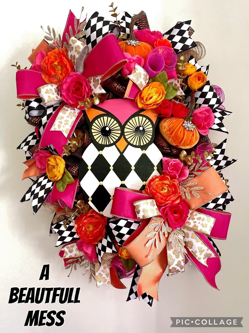 May include: A black and white checkered owl with pink accents, surrounded by pink, orange, and gold ribbon and floral accents. The wreath is decorated with small pumpkins and has the text "A Beautiful Mess" at the bottom.