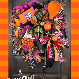 May include: A Halloween wreath with a skeleton, a black crow, a pink and orange "Trick or Treat" box, a pink and orange bow, and a black and orange leopard print ribbon.