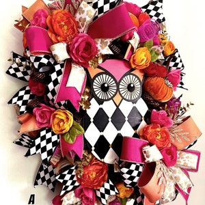 May include: A pink and black checkered owl wreath with pink, orange, and gold ribbon bows, and orange and pink flowers. The wreath has the text "A Beautiful Mess" on the bottom left corner.