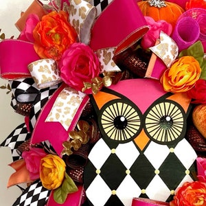 May include: A pink and black checkered owl wreath with pink, orange, and white flowers, gold glitter, and a pink bow.