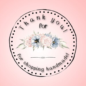 May include: A round sticker with a black dotted border and the text "Thank you for shopping handmade!" in a white font. The sticker features a floral design with pink and blue flowers.