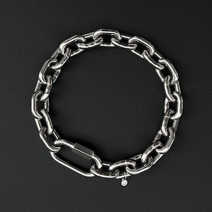 May include: A silver chain bracelet with a large carabiner clasp. The bracelet is made of thick, interlocking links and has a small charm with a smiley face. The bracelet is displayed on a black surface.