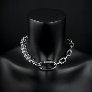May include: A silver-toned necklace with a combination of clear, round beads and a chunky chain. The necklace features a large, rectangular clasp. The jewelry is displayed on a black mannequin.