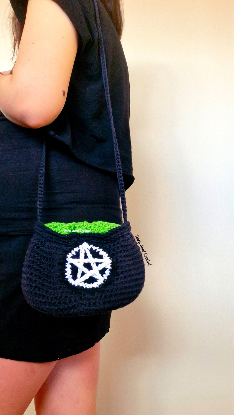 K&ouml;nnte beinhalten: Eine schwarze geh&auml;kelte Tasche mit einem wei&szlig;en Pentagramm-Design. Die Tasche hat ein gr&uuml;nes Futter und einen langen schwarzen Riemen. Die Tasche wird von einer Person getragen, die ein schwarzes Shirt tr&auml;gt.