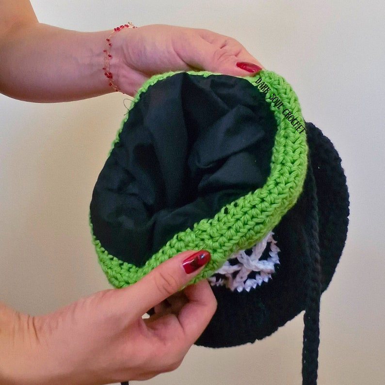 K&ouml;nnte beinhalten: Eine schwarze und gr&uuml;ne geh&auml;kelte M&uuml;tze mit einem wei&szlig;en Schneeflockenmuster. Die M&uuml;tze hat ein schwarzes Futter und einen schwarzen Kordelzug. Der Text "Dark Soul Crochet" ist auf dem Futter sichtbar.
